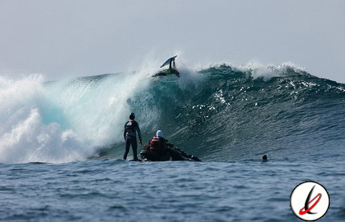 Remolcador de surf en acción con surfistas en el agua y una ola grande en el fondo.