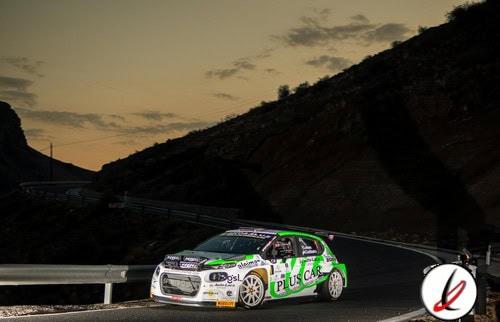 Coche de rally en curva durante una carrera en un paisaje montañoso al atardecer.