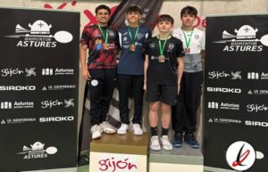 Cuatro jóvenes deportistas en el podio de un torneo de bádminton en Astures, con medallas y camisetas deportivas, en un evento en Gijón.