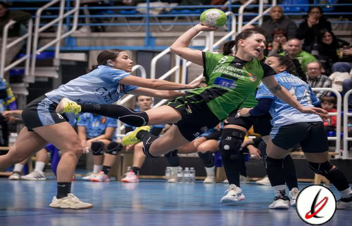 Jugadora de balonmano en acción, lanzando el balón en un partido femenino en un pabellón deportivo.