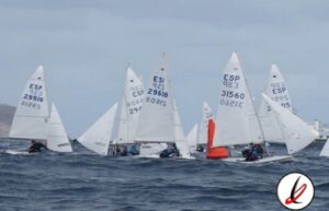 Vela ligera en competición con varios barcos navegando en el mar, con velas blancas y números visibles, bajo un cielo nublado.