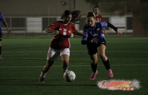 Línea 1 (ALT tag): Jugadoras de fútbol femenino en acción durante un partido nocturno en un campo de césped artificial.