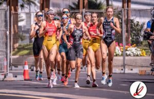 Grupo de atletas femeninas participando en una carrera en una calle de Lanzarote, con fondo de vallas y flores, en un evento deportivo al aire libre.