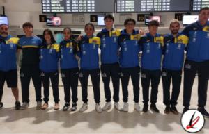 Jugadores de un equipo deportivo en aeropuerto, con uniformes azules y amarillos, posando juntos para una foto grupal antes de viajar a una competencia.