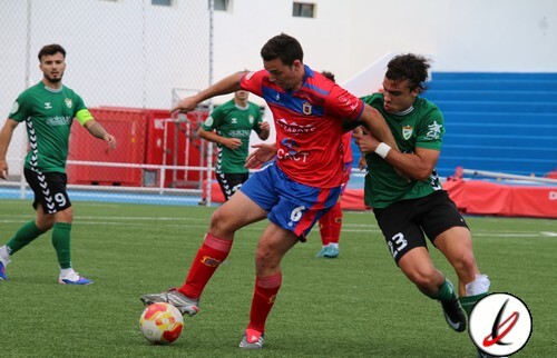 Jugadores de fútbol en acción durante un partido en un campo de césped artificial, con un jugador en camiseta roja y otros en verde, en Lanzarote.