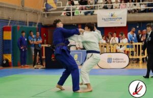 Lucha de judo entre dos competidores en un torneo en Lanzarote, con espectadores y jueces observando en el fondo.