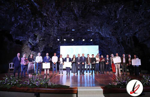 Personas en un escenario en una ceremonia de premiación en una cueva, con un grupo de individuos sosteniendo certificados y trofeos, en un evento formal y cultural.