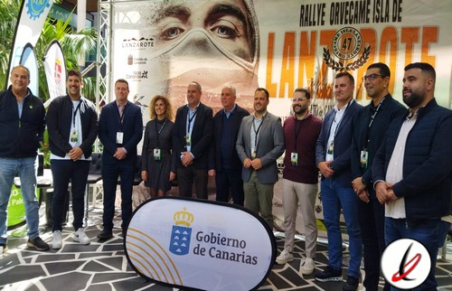 Grupo de personas en un evento deportivo en Lanzarote, con un cartel del Gobierno de Canarias y un fondo con una imagen de un rostro y texto promocional.