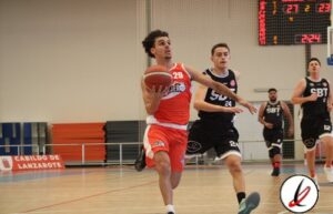 Jugador de baloncesto en acción en la cancha, con uniforme rojo y número 29, intentando anotar mientras es defendido por un oponente en uniforme negro.