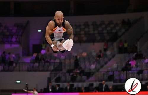 Atleta de gimnasia artística en pleno salto durante una competición en un estadio cubierto.