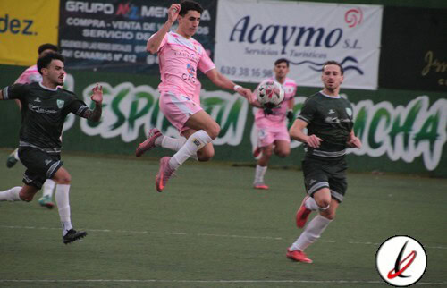 Jugadores en acción durante un partido de fútbol en un estadio, con uno en el aire intentando controlar el balón, mientras otros lo persiguen en el campo.