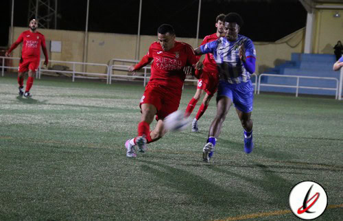 Jugadores de fútbol en acción durante un partido en un campo al aire libre, con espectadores y gradas en el fondo, en un entorno nocturno.